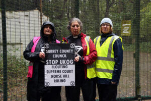 Three protesters outside the Horse Hill oil site, with a large placard reading “Surrey County Council, stop UKOG flouting Supreme Court Horse Hill ruling”